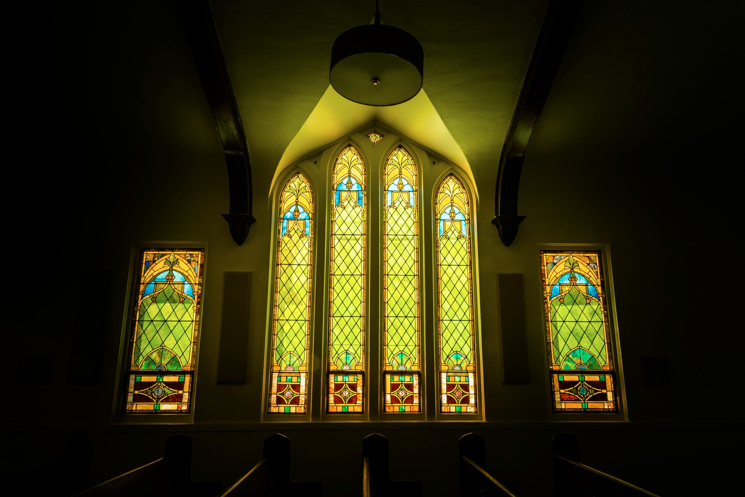 Stained glass windows inside St. Peter's Church in Humberston, featuring intricate designs with green, blue, and yellow hues, illuminated by soft interior lighting.